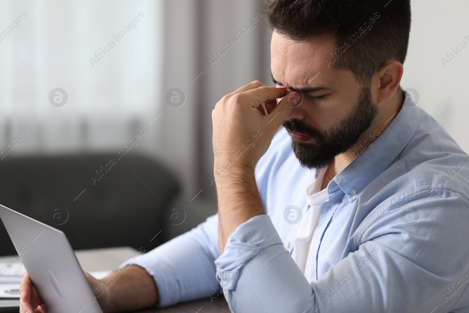 Photo of Man suffering from headache at workplace in office