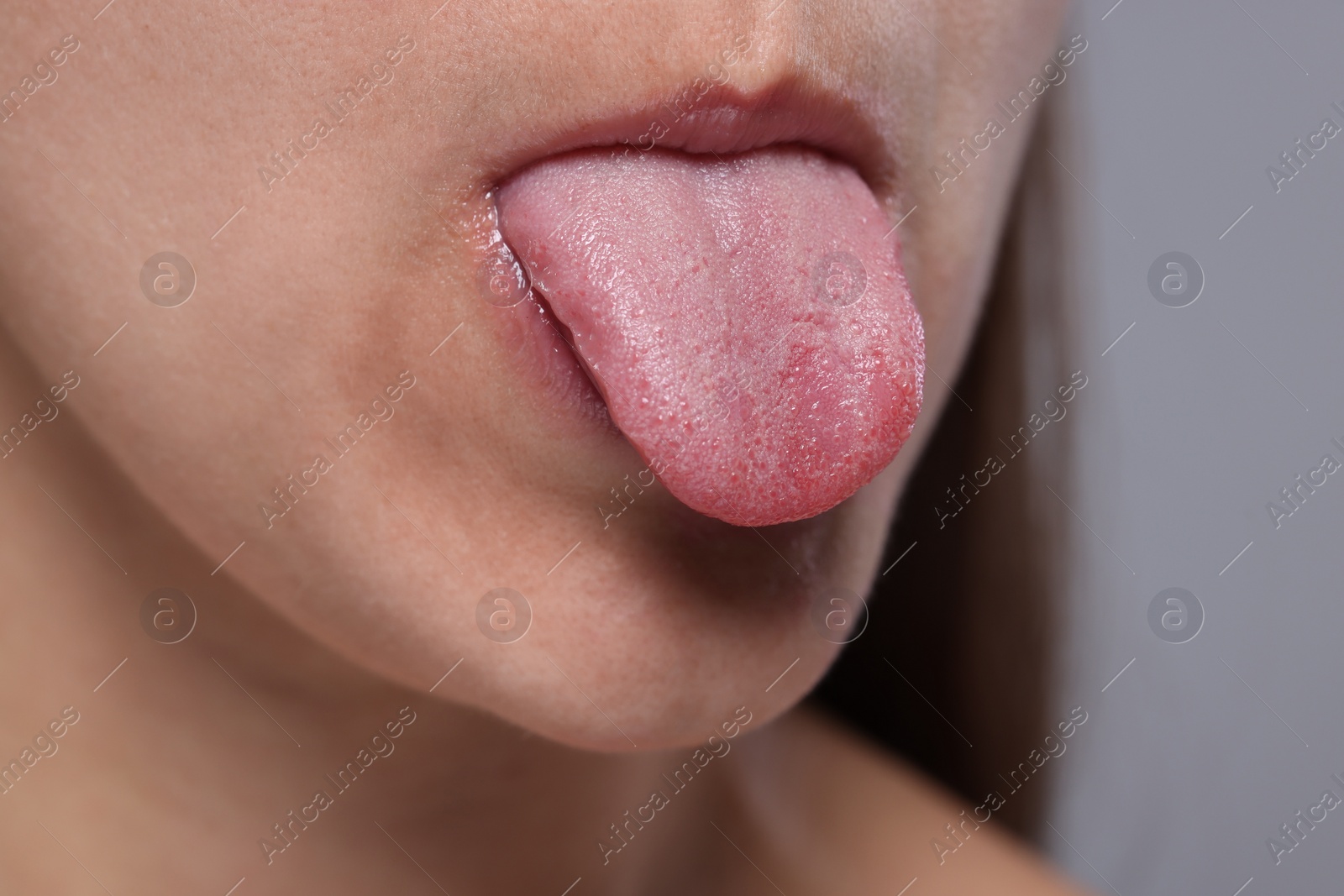 Photo of Closeup view of woman showing her tongue on grey background