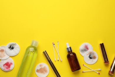 Photo of Dirty cotton pads, swabs, cosmetics and makeup removal products on yellow background, flat lay. Space for text