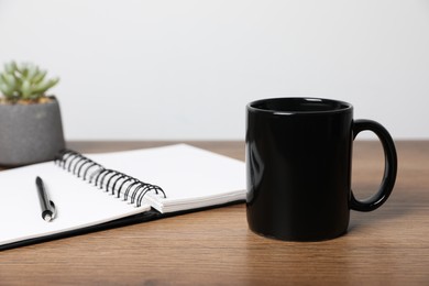 Photo of Black ceramic mug, notebook, pencil and houseplant on wooden table