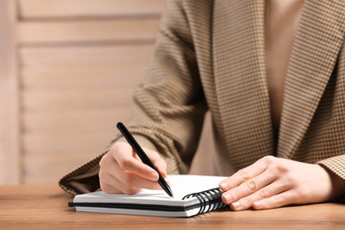 Woman writing in notebook at wooden table indoors, closeup. Space for text