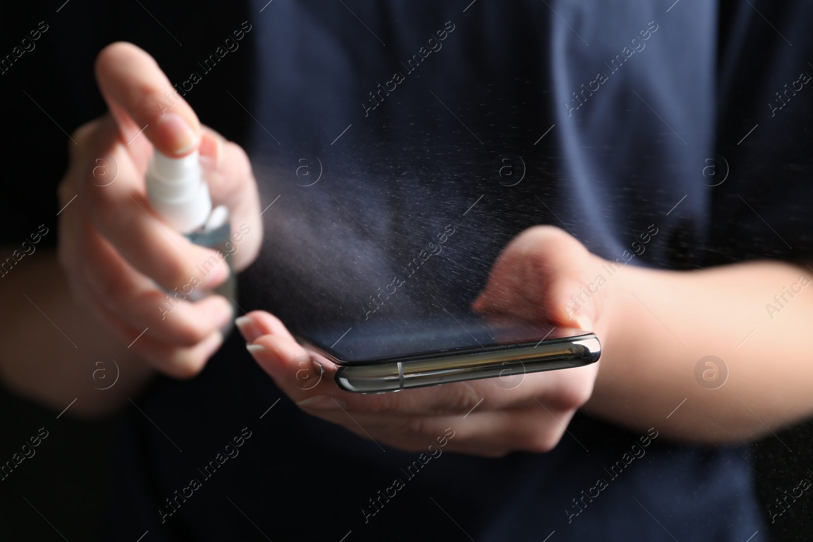 Photo of Woman spraying antiseptic onto smartphone, closeup view