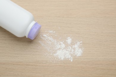 Bottle and scattered dusting powder on wooden background, top view. Baby cosmetic product