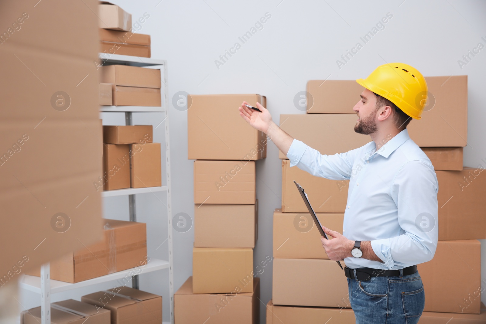 Photo of Young man with clipboard near cardboard boxes at warehouse