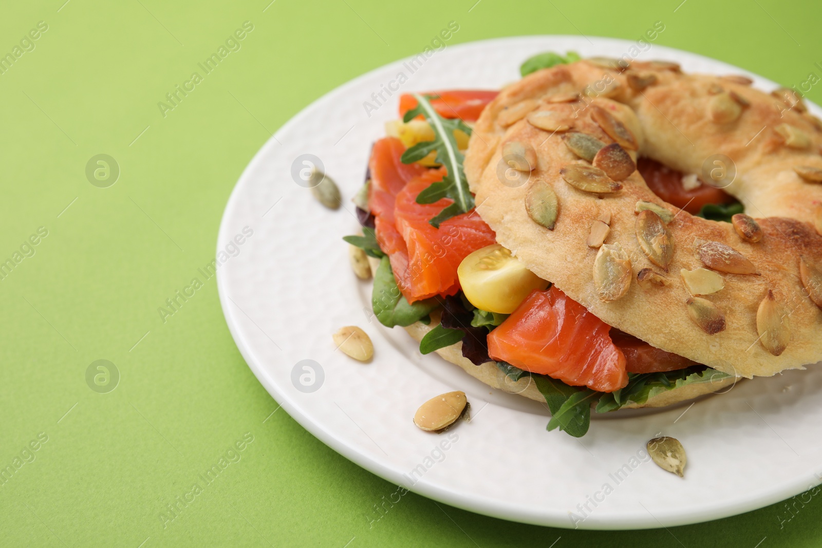 Photo of Tasty bagel with salmon and tomatoes on light green background, closeup. Space for text