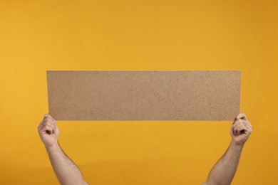 Photo of Man holding blank cardboard banner on orange background, closeup. Space for text
