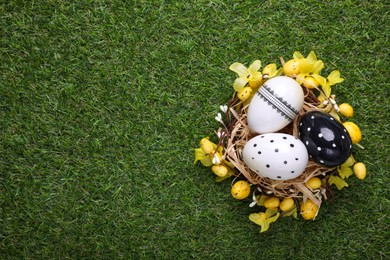 Photo of Festively decorated Easter eggs on green grass, top view. Space for text