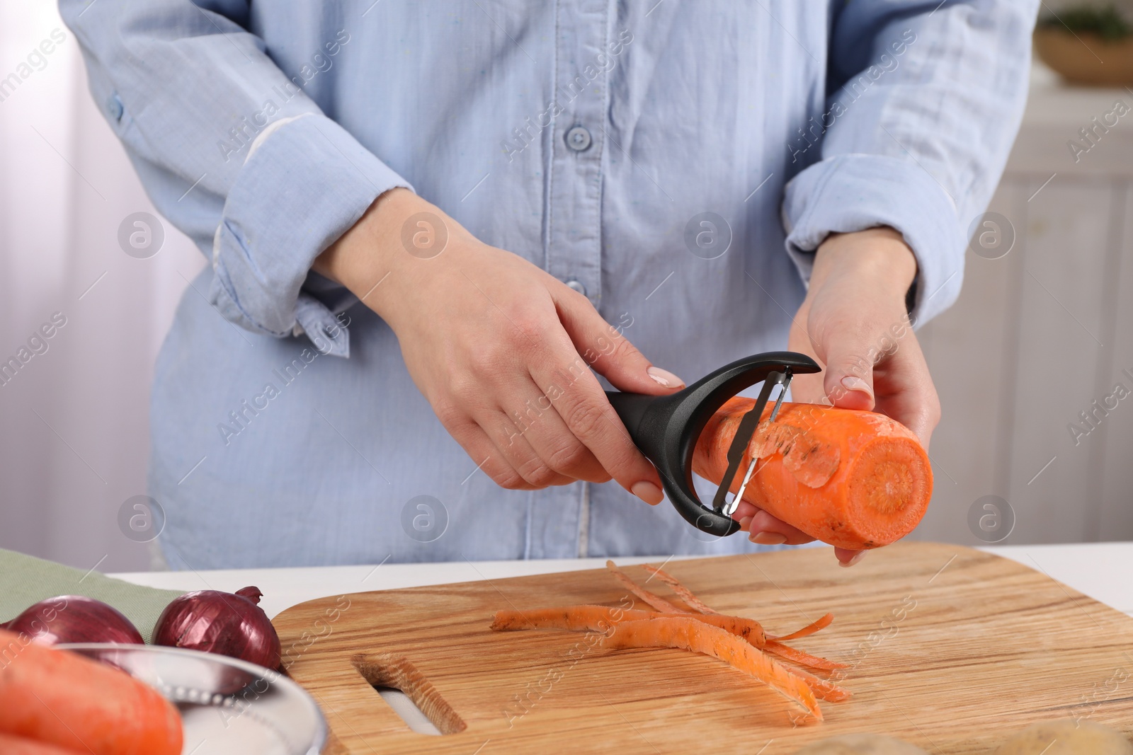 Photo of Woman peeling fresh carrot at table indoors, closeup