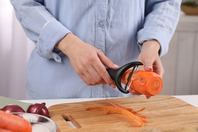 Woman peeling fresh carrot at table indoors, closeup