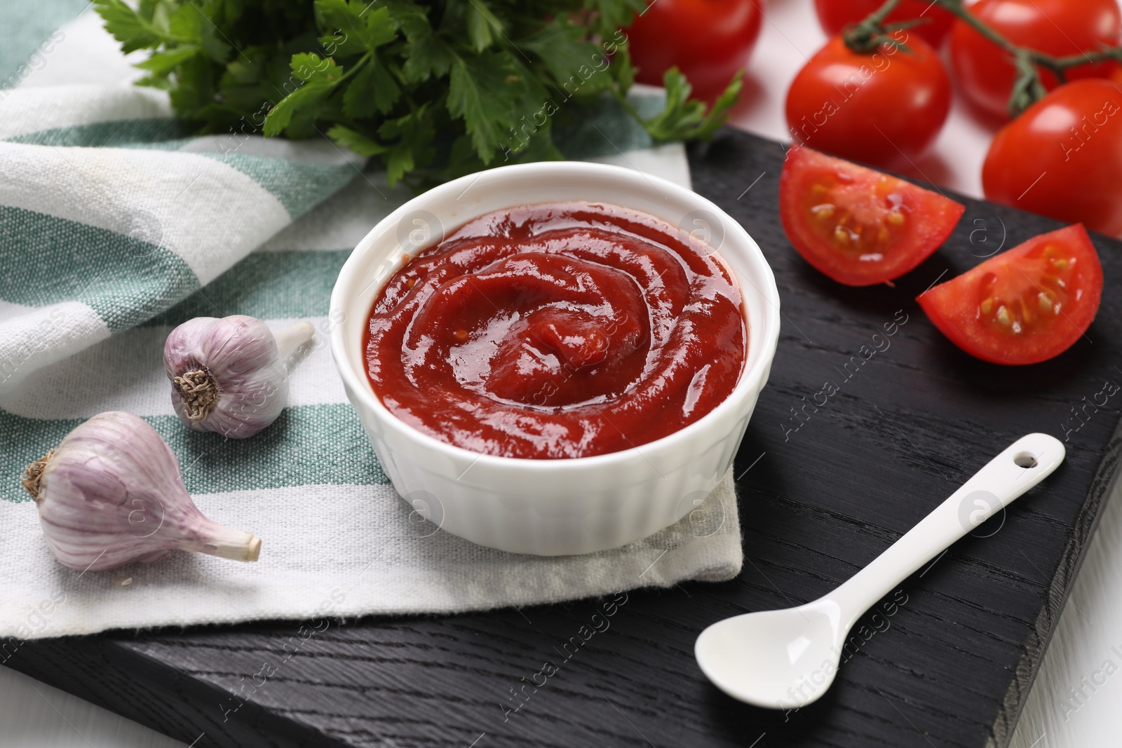 Photo of Organic ketchup in bowl, fresh tomatoes and garlic on table. Tomato sauce