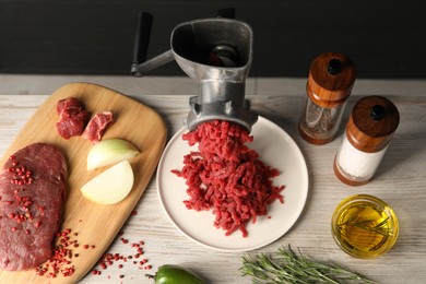 Metal meat grinder with minced beef and spices on light wooden table