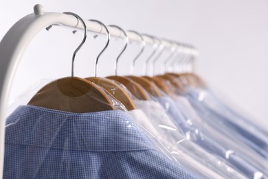 Photo of Hangers with shirts in dry cleaning plastic bags on rack against light background, closeup. Space for text