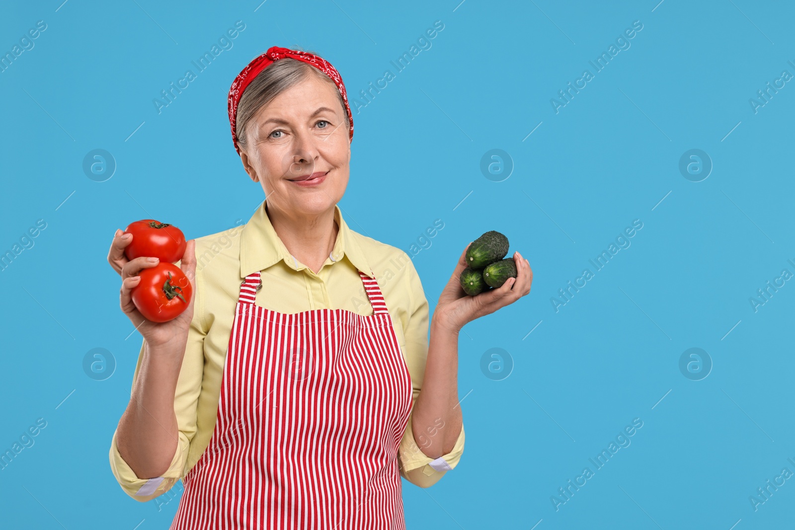 Photo of Happy housewife with tomatoes and cucumbers on light blue background, space for text