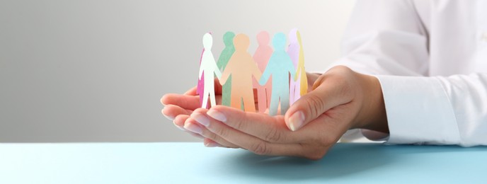 Woman holding paper human figures at table, closeup. Diversity and Inclusion concept