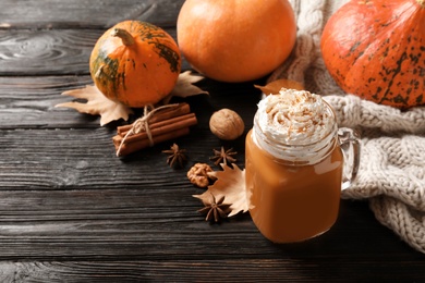 Photo of Mason jar with tasty pumpkin spice latte and space for text on wooden table