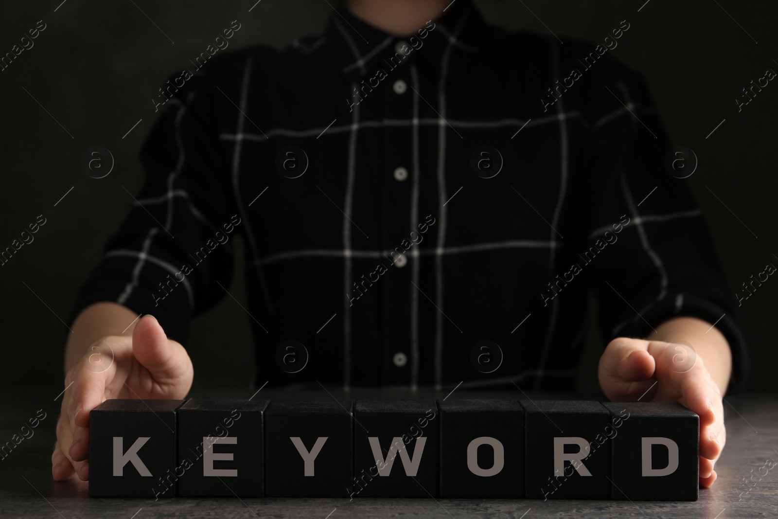Photo of Woman demonstrating black cubes with word KEYWORD at grey table, closeup