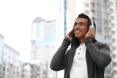 Handsome young African-American man with headphones listening to music on city street. Space for text