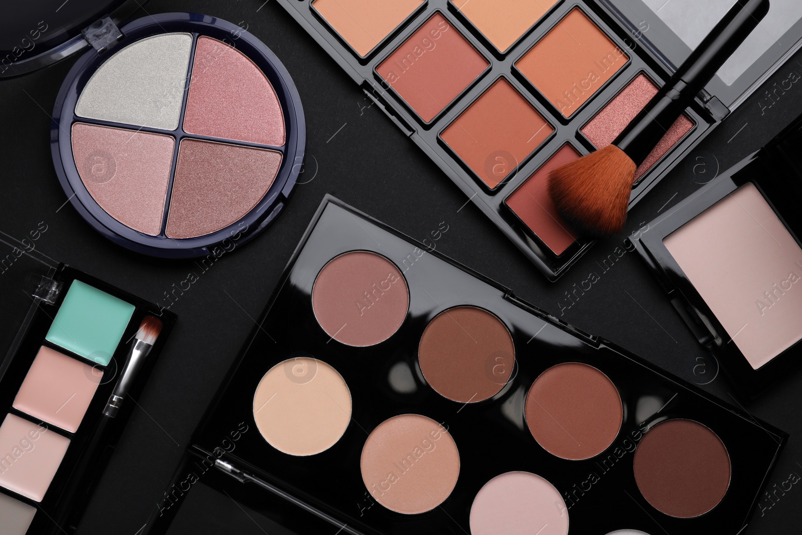 Photo of Different contouring palettes and brush on black background, flat lay. Professional cosmetic product
