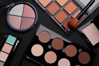 Different contouring palettes and brush on black background, flat lay. Professional cosmetic product