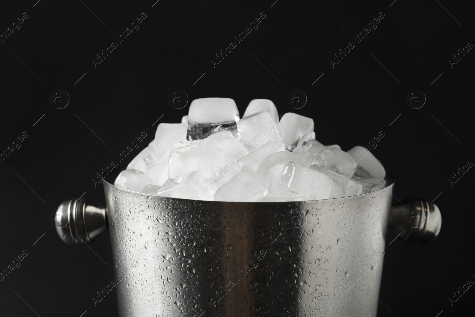 Photo of Metal bucket with ice cubes on dark background, closeup