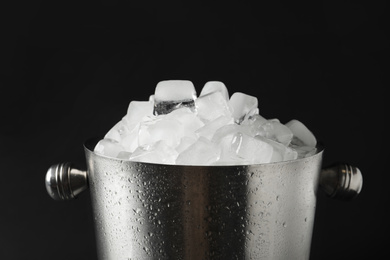 Photo of Metal bucket with ice cubes on dark background, closeup