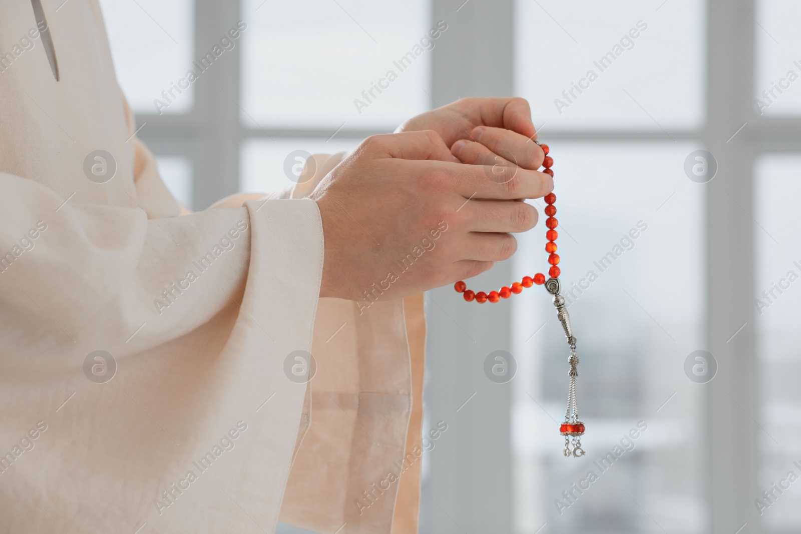 Photo of Muslim man with misbaha praying near window indoors, closeup. Space for text