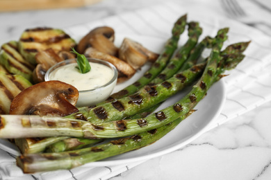 Tasty grilled asparagus served with sauce and mushrooms on plate, closeup