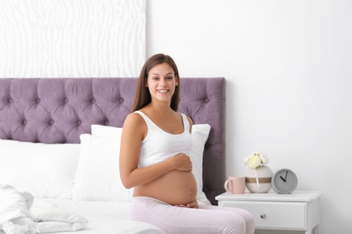 Happy pregnant woman sitting on bed at home