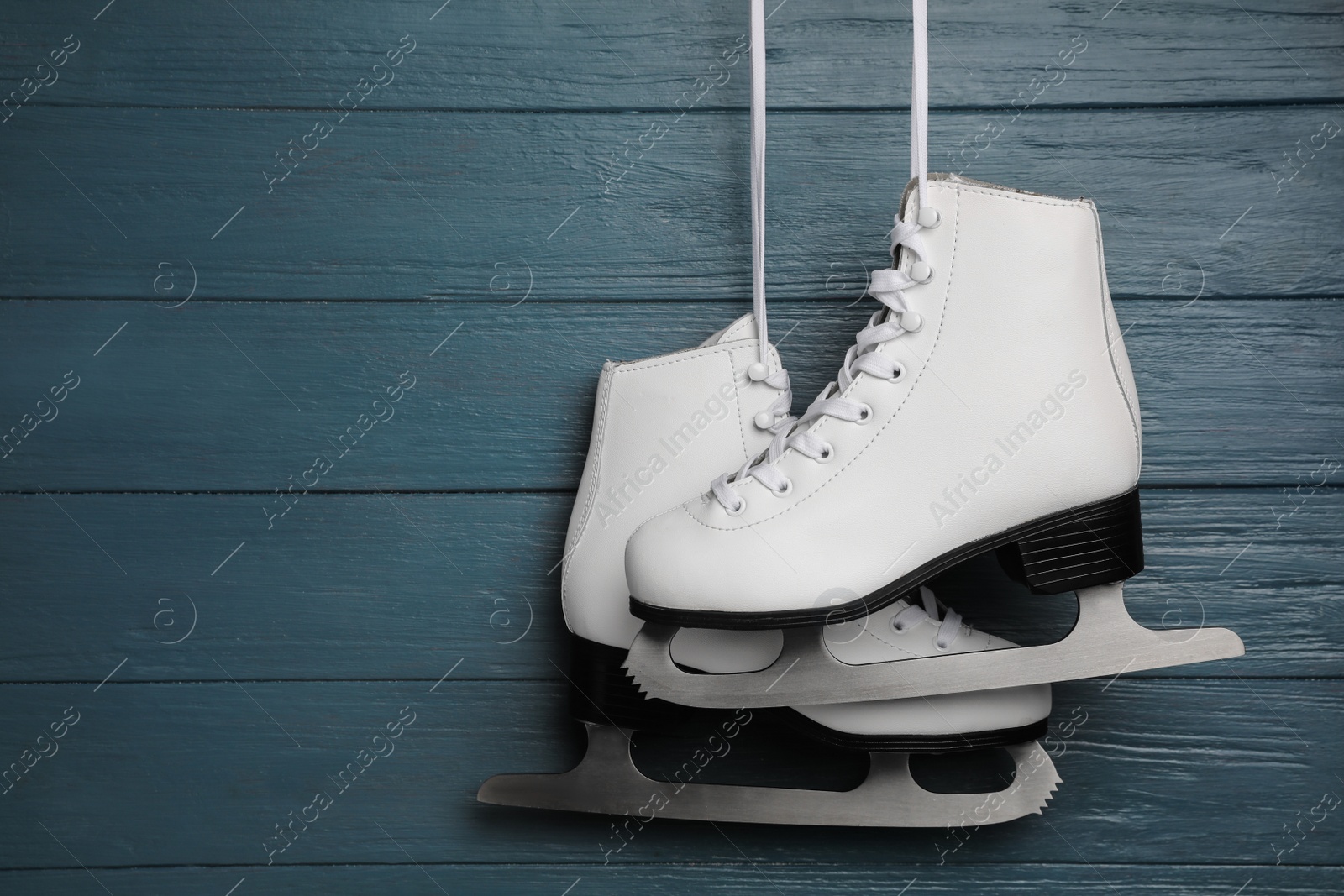 Photo of Pair of white ice skates hanging on blue wooden background. Space for text