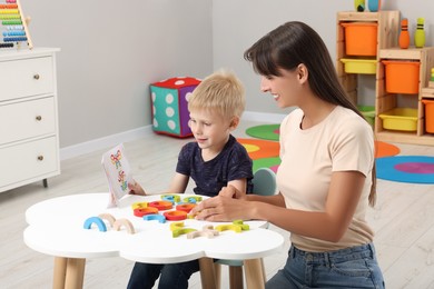 Photo of Motor skills development. Happy mother helping her son to play with colorful wooden arcs at white table in room