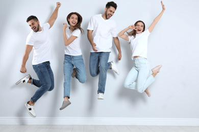 Group of young people in stylish jeans jumping near light wall