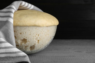 Photo of Bowl of fresh yeast dough on grey wooden table, closeup. Space for text