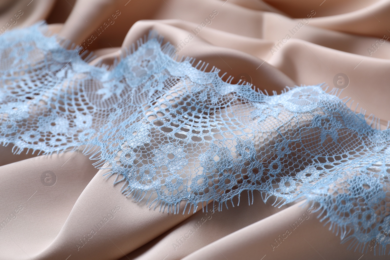 Photo of Beautiful light blue lace on beige fabric, closeup