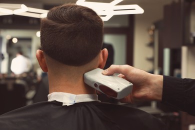 Photo of Professional hairdresser making stylish haircut in salon, back view