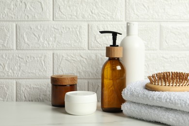 Photo of Different bath accessories and personal care products on white table near brick wall