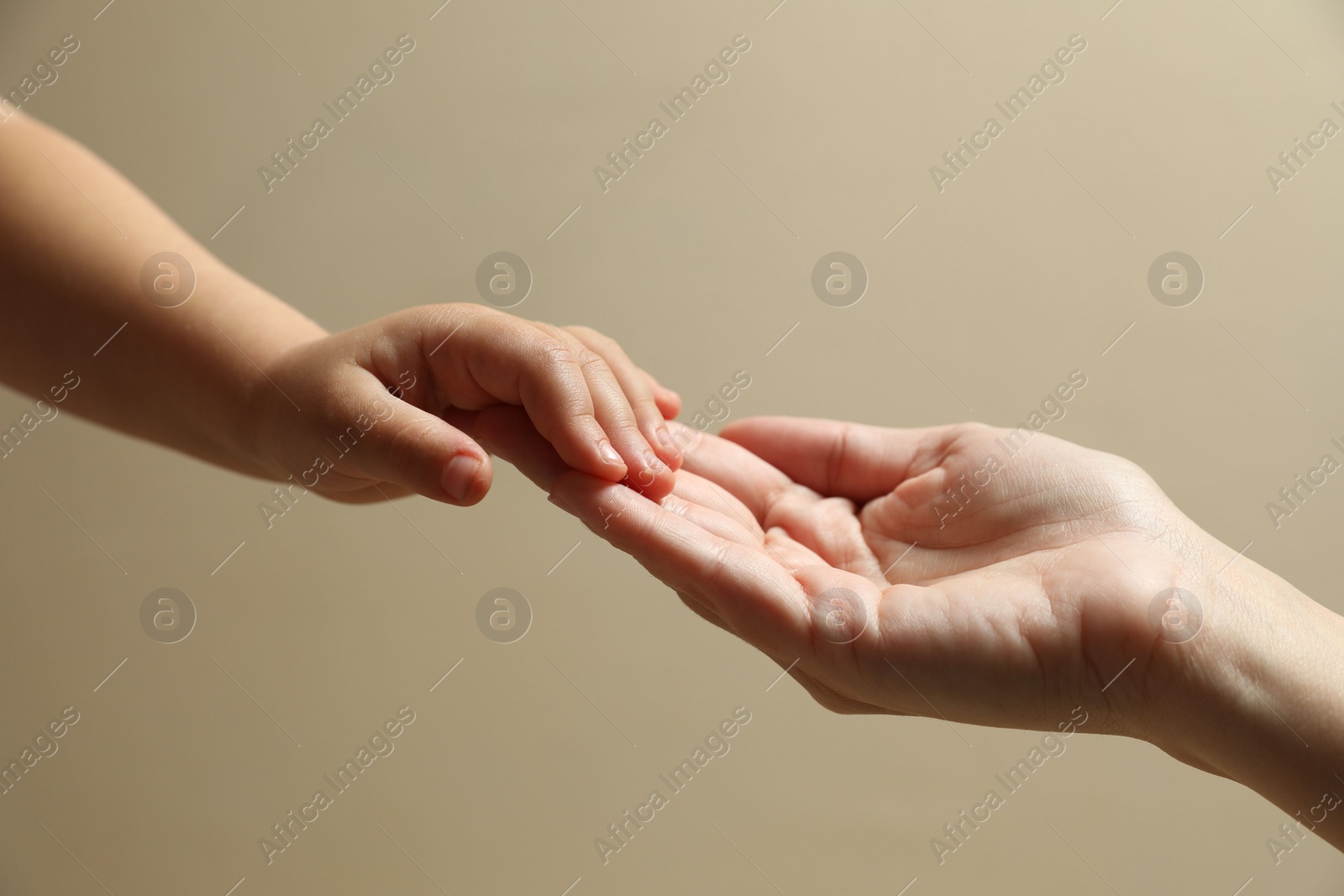 Photo of Mother and child holding hands on beige background, closeup