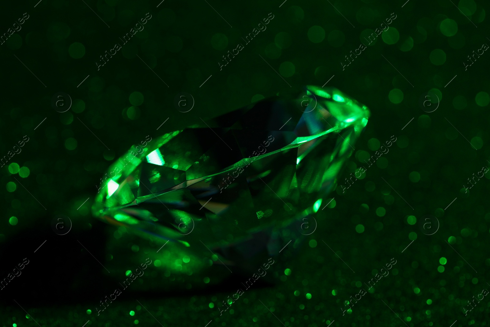 Photo of Beautiful dazzling diamond on green glitter surface, closeup