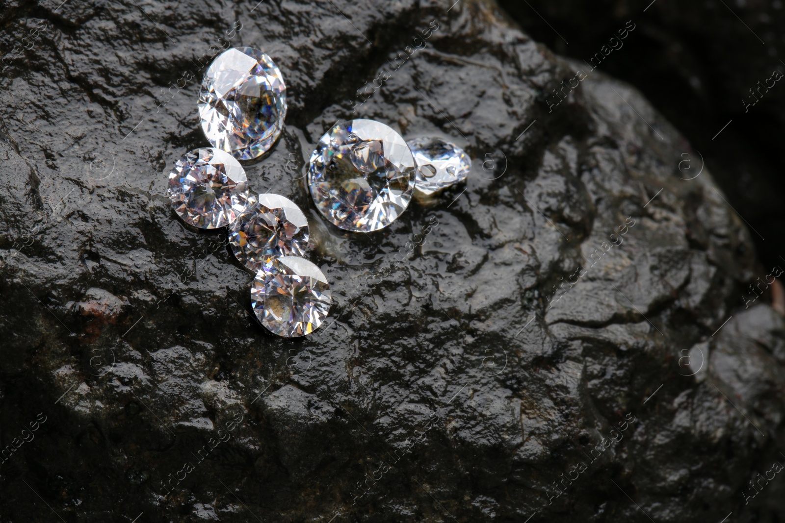 Photo of Different shiny diamonds on wet stone surface. Space for text