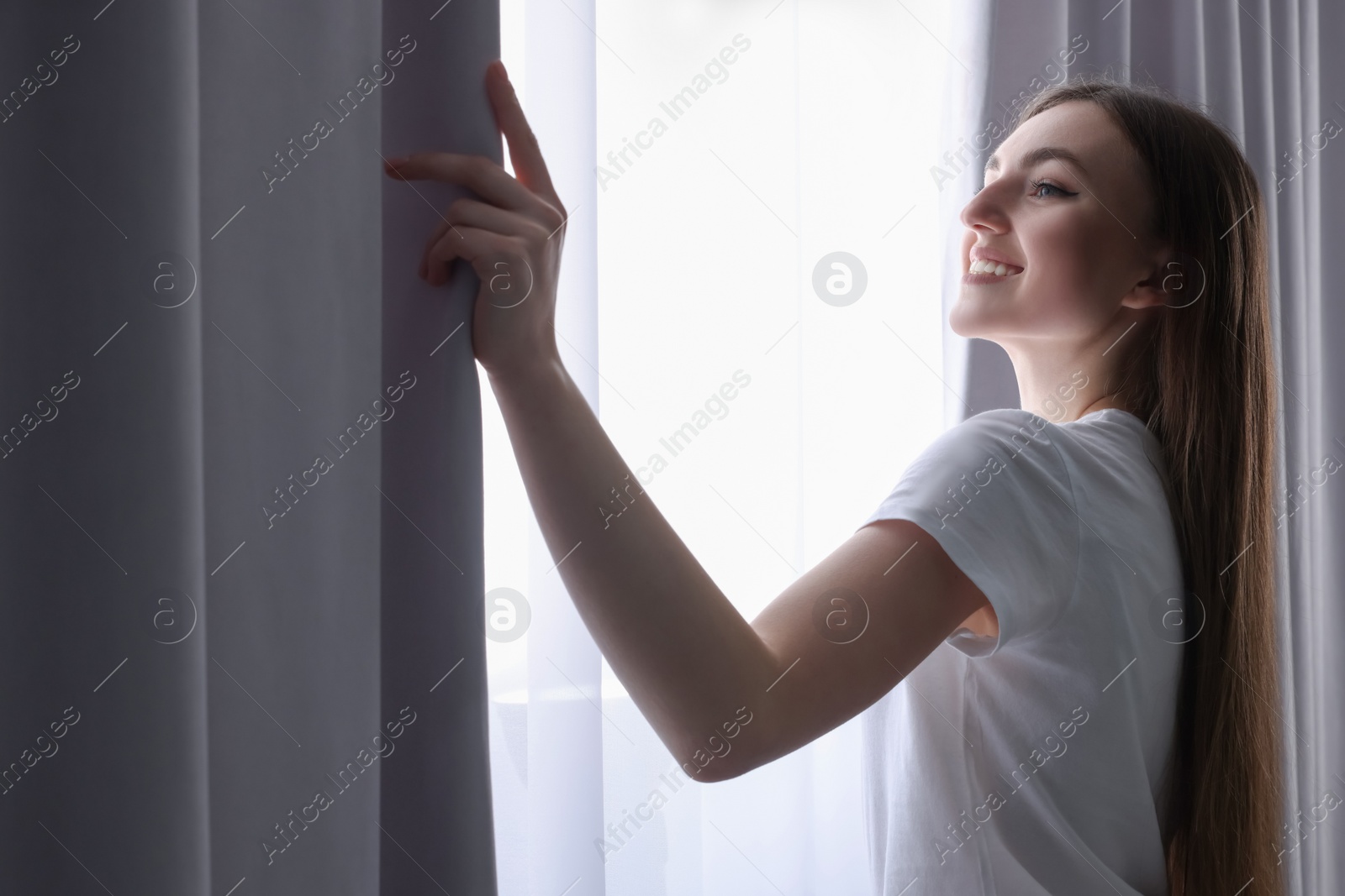 Photo of Happy woman opening stylish curtains at home