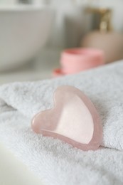 Photo of Rose quartz gua sha tool with soft towel on white table, closeup