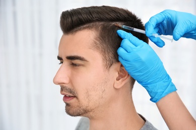 Young man with hair loss problem receiving injection on blurred background