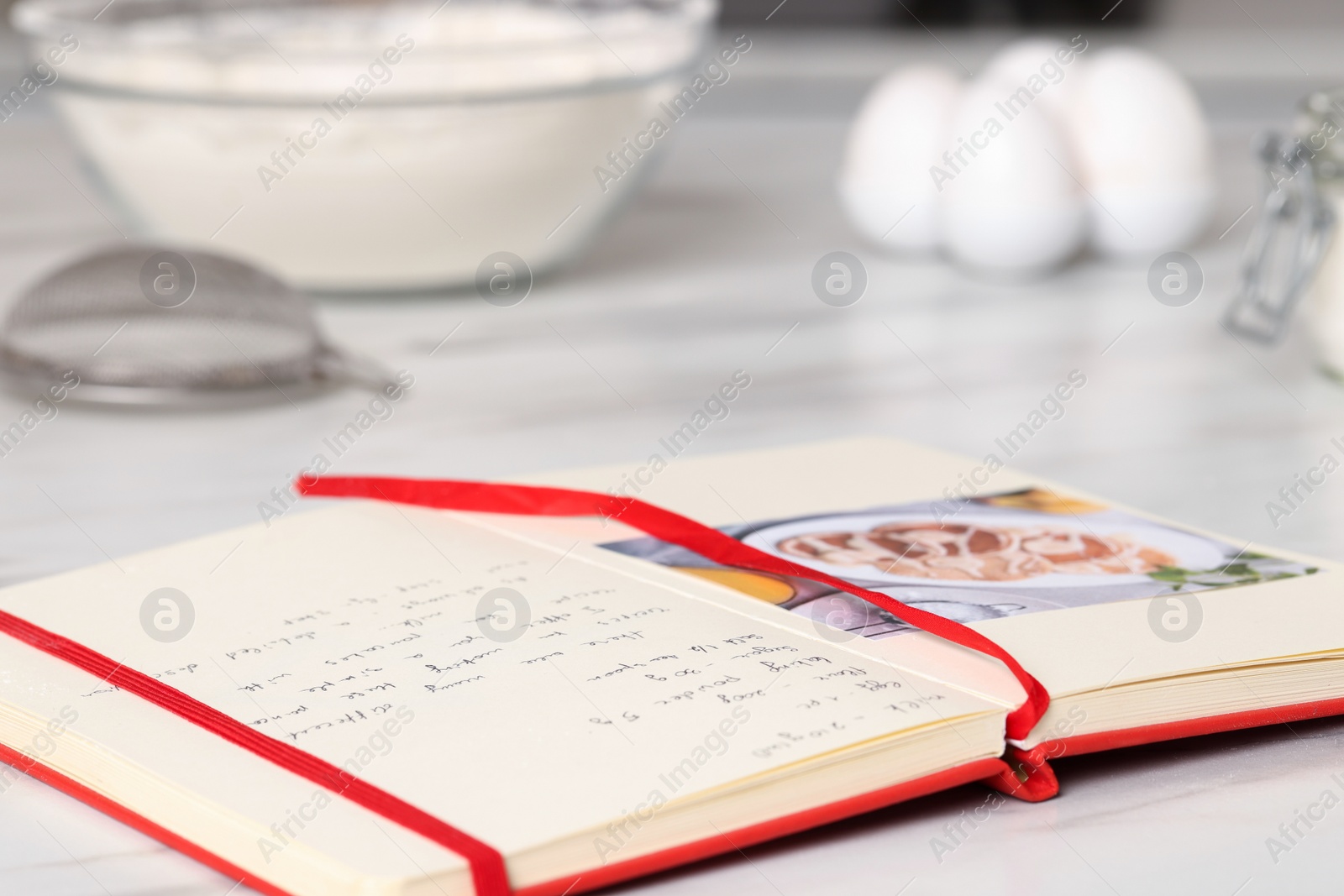 Photo of Open recipe book on white marble table in kitchen, closeup. Space for text