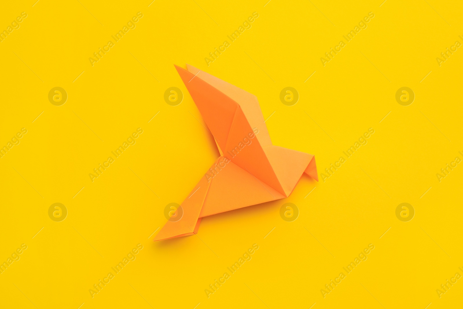 Photo of Origami art. Beautiful handmade paper bird on yellow background, top view