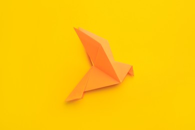 Origami art. Beautiful handmade paper bird on yellow background, top view