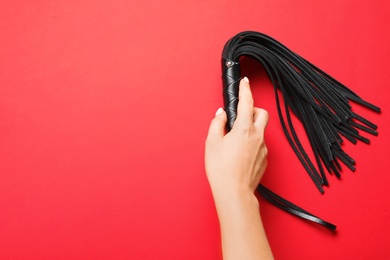 Young woman holding black whip for sexual role play on red background, top view with space for text