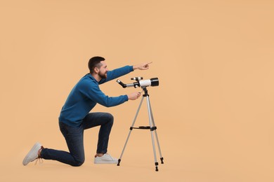 Photo of Happy astronomer with telescope pointing at something on beige background. Space for text