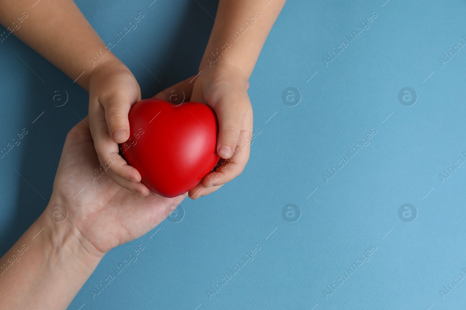 Photo of Mother and her child holding red decorative heart on light blue background, top view. Space for text