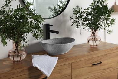 Photo of Eucalyptus branches and towel near stylish vessel sink on bathroom vanity. Interior design