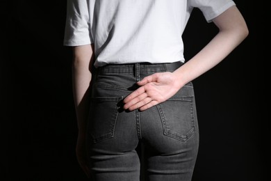 Woman showing open palm behind her back on black background, back view