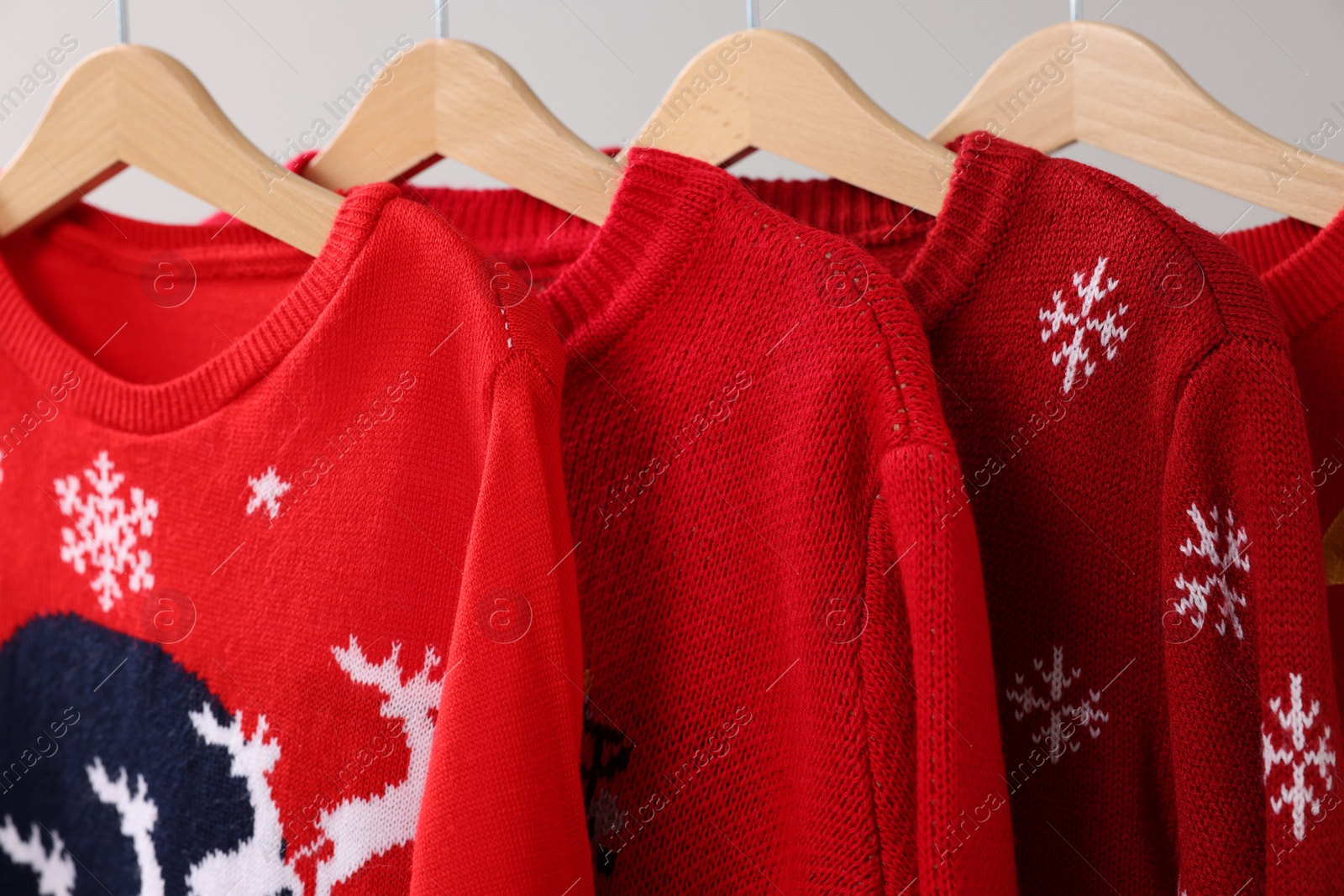 Photo of Different Christmas sweaters hanging on rack against light background, closeup